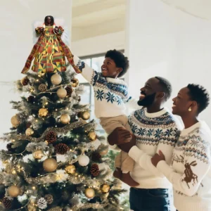Heartwarming Christmas moment: father helps boy put a kente black angel tree topper while mother looks on smiling