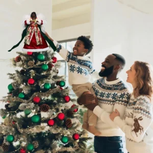 Heartwarming Christmas moment: father helps boy put a red black angel tree topper while mother looks on smiling